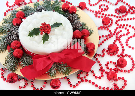 Gâteau de Noël avec du glaçage et des baies de houx, verdure d'hiver couvert de neige, boules rouges, de perles et de ruban à l'archet. Banque D'Images