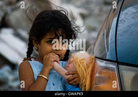 Sur, Oman, le 22 octobre 2013 : Little girl omanais debout sur une voiture tenant une poupée, en me regardant dans l'appareil photo Banque D'Images