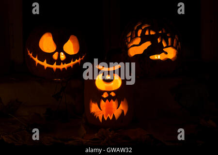 Composition Photo de trois citrouilles pour l'Halloween. Jack, un Cyclope et les mains de la citrouille contre les feuilles d'automne et des bougies Banque D'Images