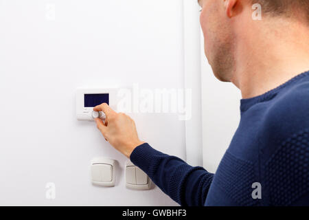 Les hommes règlent la température sur le tableau de contrôle du chauffage central au mur dans la salle de séjour. Banque D'Images