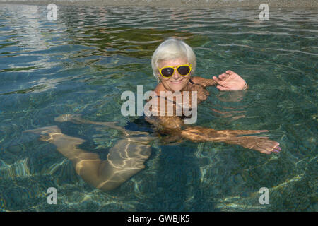 Portrait de senior lady c'est couché dans l'eau clair transparent de la plage de la mer de galets. Banque D'Images