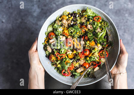 Un grand bol de salade de poulet au sud-ouest de l'avocat dans une vinaigrette crémeuse woman's hands est photographié à partir de la vue supérieure. Banque D'Images