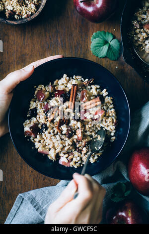 A womans mains sont photographiés comme elle est sur le point de manger un bol de petit-déjeuner chaud Farro bol avec des pommes à la cannelle. Banque D'Images