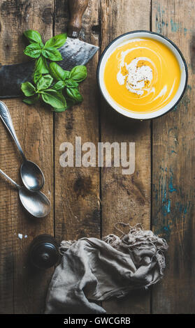 Crème de potiron soupe dans un bol avec le basilic et les épices sur fond de bois rustique ancien, vue du dessus, copiez l'espace, composition verticale Banque D'Images