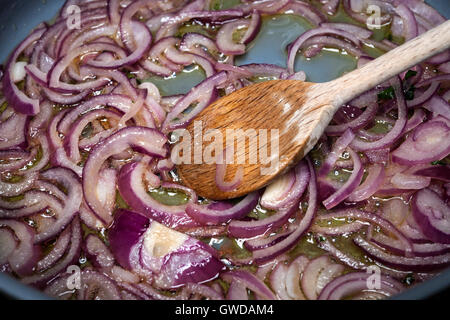 Sauteing en remuant les oignons rouges avec cuillère en bois dans la casserole, gros plan Banque D'Images