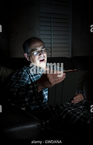 Le bâillement middle aged man wearing pajamas Tablette de lecture la nuit au lit Banque D'Images