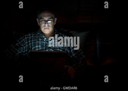 Middle aged man wearing pajamas Tablette de lecture la nuit au lit avec de graves et d'expression inquiète, copy space Banque D'Images