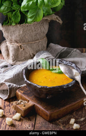 Bol en céramique de carottes, servi avec du basilic frais, croûtons, essuie-tout et la cuillère sur la vieille chaise en bois. Style rustique foncé Banque D'Images