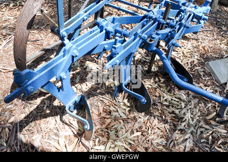 Libre d'une vieille ferme en métal bleu avec des lames machines de travail du sol et les pièces rouillées reposant sur une surface au sol de feuilles séchées. Banque D'Images