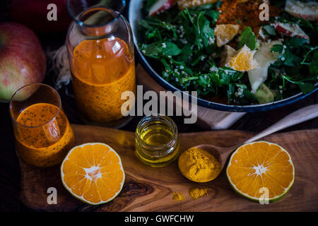 Orange curcuma vinaigrette aux graines de pavot dans une bouteille et un verre, servi avec un bol de salade, moitié orange, une pomme, le curcuma et Banque D'Images