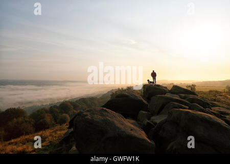 Un homme et son chien voir le lever du soleil sur la vallée de la Wharfe haut de Otley Chevin, la vallée ci-dessous rempli de cloud,Otley Chevin, Leeds, Angleterre, RU Banque D'Images