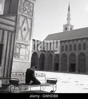 Années 1950, historiques, prière de l'après-midi, les pieds nus à l'extérieur représentant arabe sur un banc métallique à genoux avec la tête inclinée d'effectuer la salat ou la prière. Banque D'Images