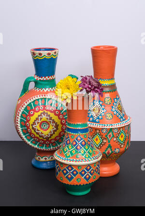 Studio shot of still life de trois vases en poterie décorée orange avec deux fleurs jaune et violet dans un contexte de tableau noir Banque D'Images