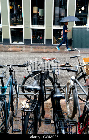 Homme marchant sous la pluie à côté d'un parc de vélo, Copenhague, Danemark Banque D'Images