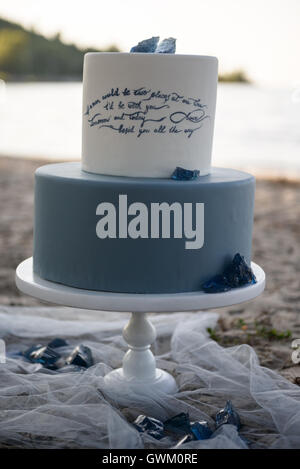 Gâteau de mariage bleu à deux niveaux sur une plage de sable, décoré de pierres bleues. Gâteau de mariage sur le sable au coucher du soleil Banque D'Images