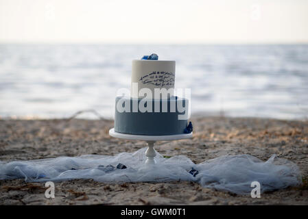 Gâteau de mariage bleu à deux niveaux sur une plage de sable, décoré de pierres bleues. Gâteau de mariage sur le sable au coucher du soleil Banque D'Images