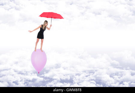 Fille aux pieds nus sur un ballon, elle reste en équilibre avec un parapluie rouge tout en volant au-dessus des nuages blancs dans un ciel bleu Banque D'Images