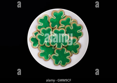 Shamrock shaped shortbread cookies avec sucre vert arrose sur une plaque sur fond noir Banque D'Images