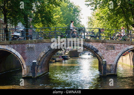 Les cyclistes traversent un soleil d'été pont-canal à Amsterdam. Banque D'Images