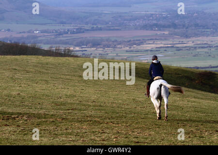 Femme chevauchant le cheval blanc le long de la crête de South Downs près de Firle Beacon en hiver, South Downs National Park, East Sussex, Angleterre, Royaume-Uni Banque D'Images