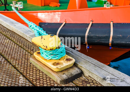 Borne lumineuse jaune vert serré avec corde à un bateau rouge. Banque D'Images