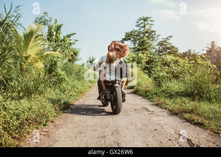 Vue arrière du jeune couple riding on rural road. Femme avec son petit ami équitation en moto sur une journée d'été. Banque D'Images