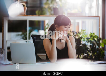 Shot of young woman sitting at office 24 documents et souriant. Asian business woman en passant par des formalités administratives de son Banque D'Images