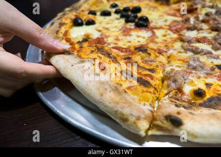 Mains d'une femme prenant une tranche de pizza Banque D'Images