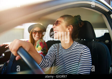 Smiling young woman un ascenseur dans sa voiture en ville, vue de profil par la fenêtre côté ouvert avec sun flare Banque D'Images