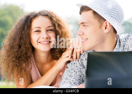 Couple lying together in a park with laptop Banque D'Images