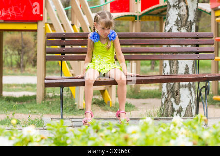 Crying Girl assis sur le banc en arrière-plan de l'aire de jeux Banque D'Images