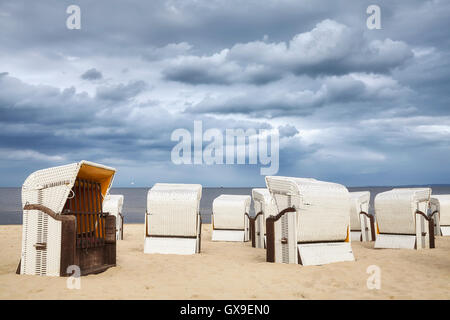 Nuages de pluie sur le panier en osier chaises sur une plage vide. Banque D'Images