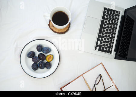Travailler au lit , coffre et tasse de café sur le lit blanc, la lumière du matin Banque D'Images