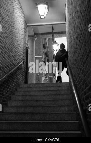 Fille au sommet des escaliers à la sortie d'un métro éclairé par des lampes suspendues au plafond. Images en noir et blanc. Banque D'Images