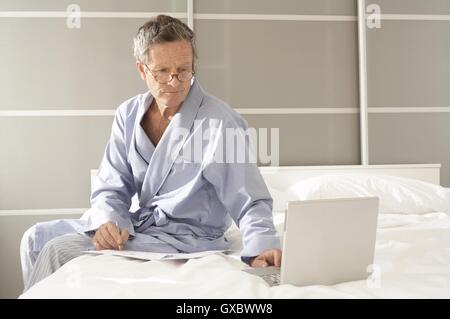 Senior man sitting on bed vérification sur l'ordinateur portable Banque D'Images