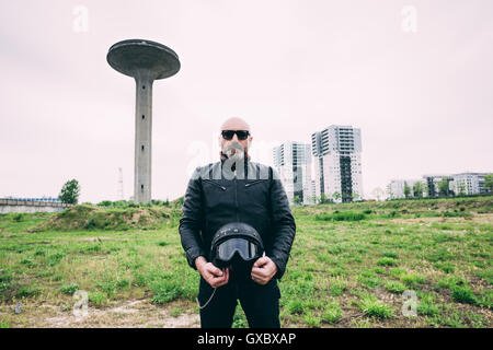 Portrait of mature male motorcyclist standing on wasteland holding helmet Banque D'Images