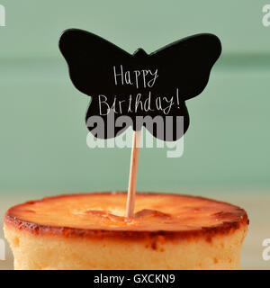 Libre d'un cheesecake surmontée d'une pancarte en forme de papillon noir avec le texte joyeux anniversaire écrit en C, contre un rus Banque D'Images