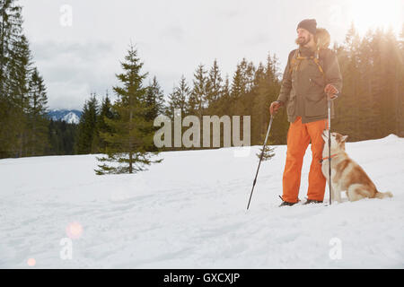 Mid adult man en raquettes, le chien à côté de lui, Elmau, Bavière, Allemagne Banque D'Images