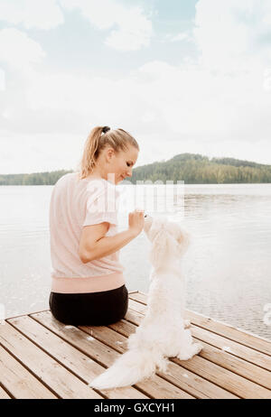 Woman petting dog on Coton de Tuléar, jetée du lac Orivesi, Finlande Banque D'Images