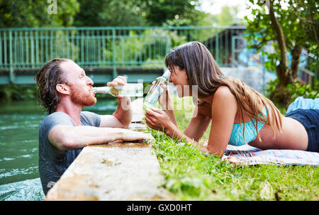 Jeune homme dans la rivière, young woman lying on grass au bord de rivière, l'homme de boire de bière bouteille Banque D'Images