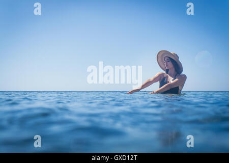 Young woman wearing sunhat patauger dans la mer d'un bleu profond, Villasimius, Sardaigne, Italie Banque D'Images