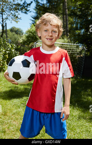 Portrait of boy wearing uniformes de soccer holding soccer ball in garden Banque D'Images