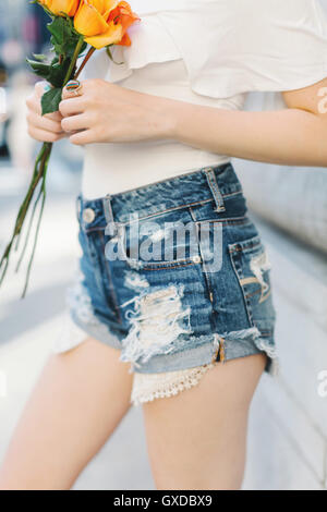 Jeune femme portant un short en jean coupé, holding roses, mid section Banque D'Images