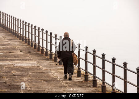 Homme mûr en marchant le long du brise-lames Heugh à Hartlepool, Angleterre pour une journée de pêche en dépit de l'épais brouillard Banque D'Images