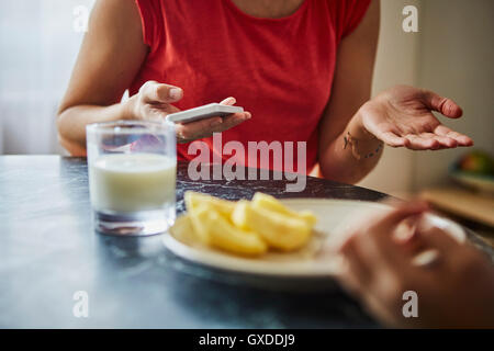 Portrait de femme à table à manger holding smartphone Banque D'Images