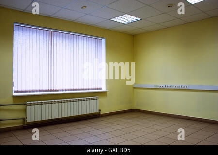 Coin de bureau vide avec étage de pierres, plafond, luminaires, murs jaunes, et avec la fenêtre fermée de jalousie Banque D'Images