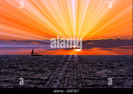 Coucher du soleil voilier est un bateau naviguant le long de la silhouette de l'eau de l'océan avec une rafale de rayons x qui s'écoule derrière les nuages Banque D'Images