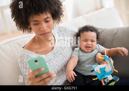 Mother holding baby son pleurer tout en texting on cell phone Banque D'Images