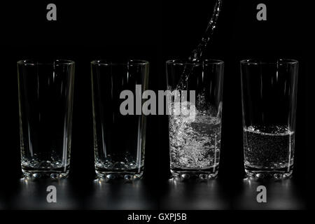 Verre à quatre de l'eau propre est versé sur un fond sombre Banque D'Images
