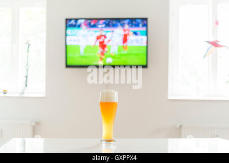 Joueur de football à la télévision et d'un verre de bière de blé sur une table Banque D'Images